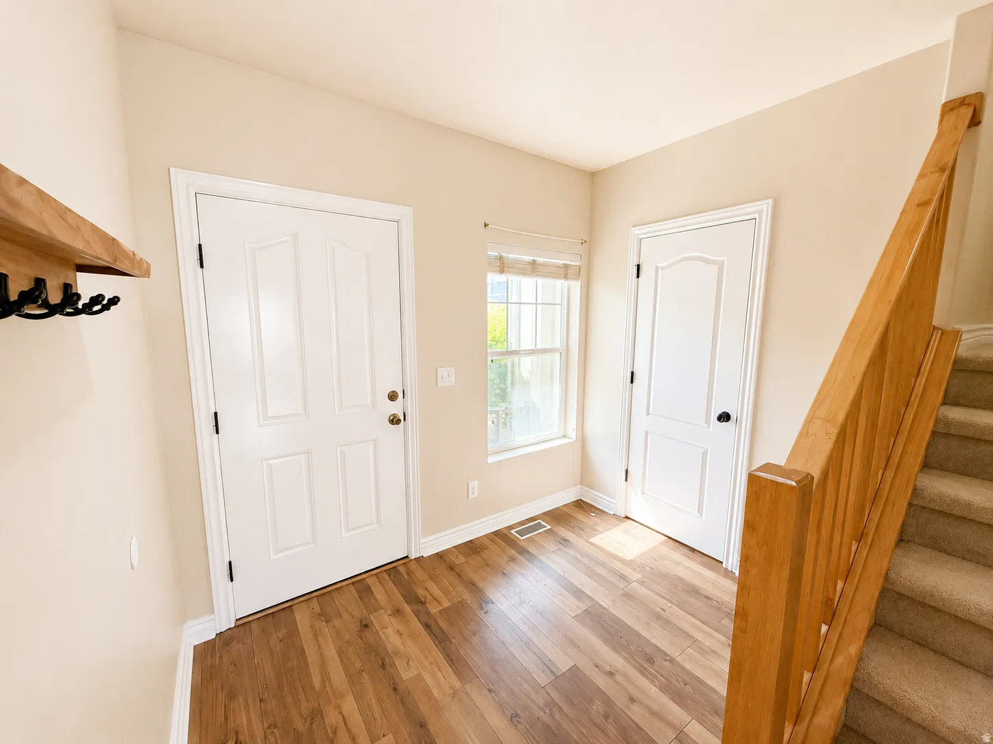 Entryway featuring wood-finish flooring, a white paneled front door, a light wood railing, and a window with a roman shade