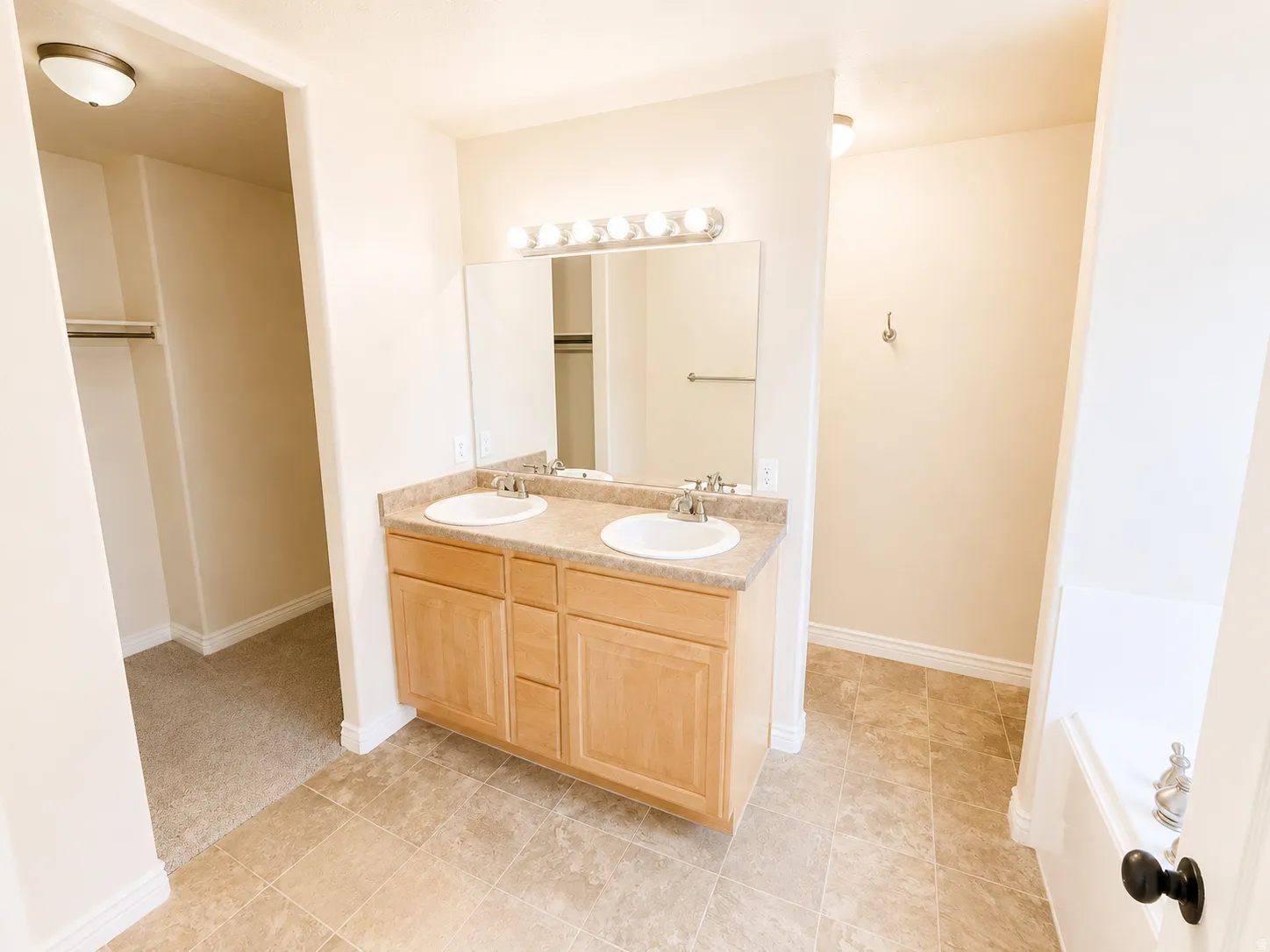 Bathroom featuring a dual-sink vanity with a light wood-finish cabinet, a large framed mirror, and a five-light vanity fixture