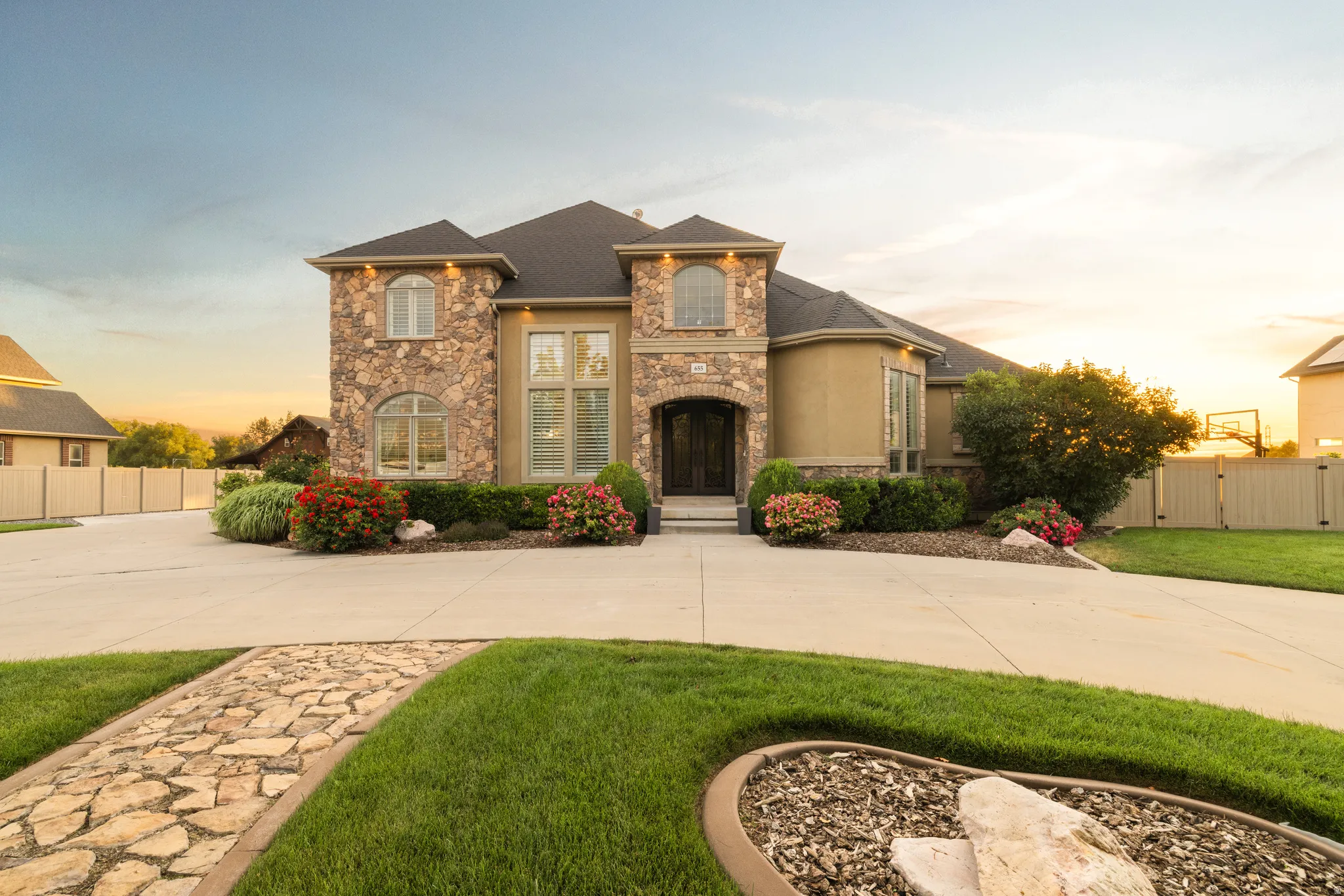 Stately residence featuring a stone and stucco exterior, arched window accents, a dark shingle roof, and a meticulously landscaped front yard