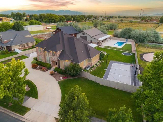 Expansive property featuring a stone and stucco exterior, a large paved driveway, a dedicated sport court, an inground swimming pool, and a separate outbuilding with a covered patio
