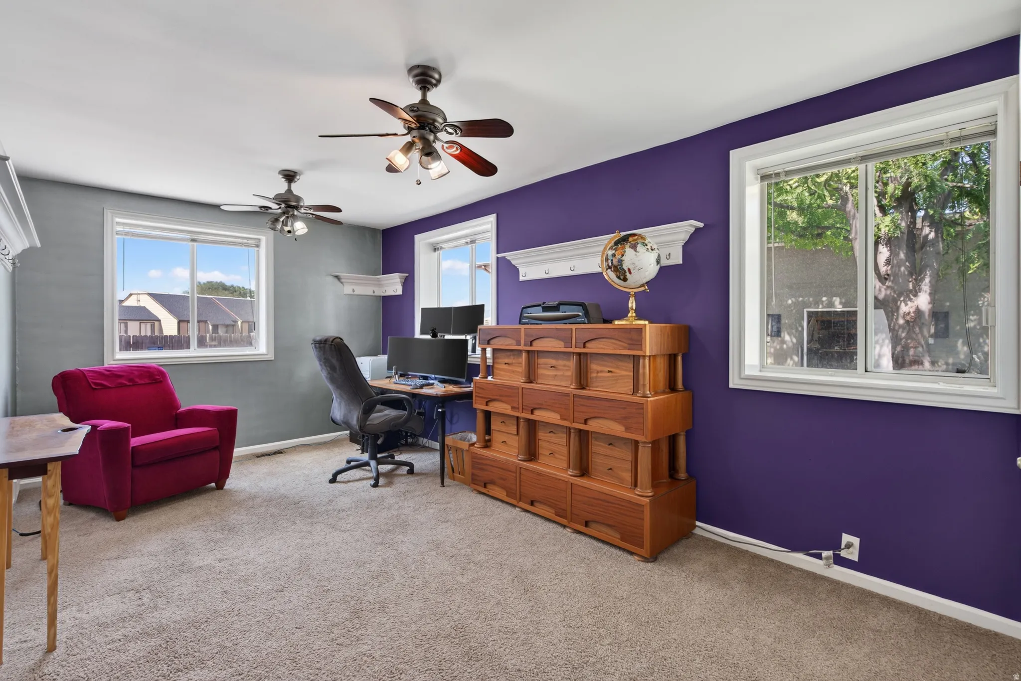 Carpeted room featuring multiple windows, two ceiling fans with lighting, and white baseboards