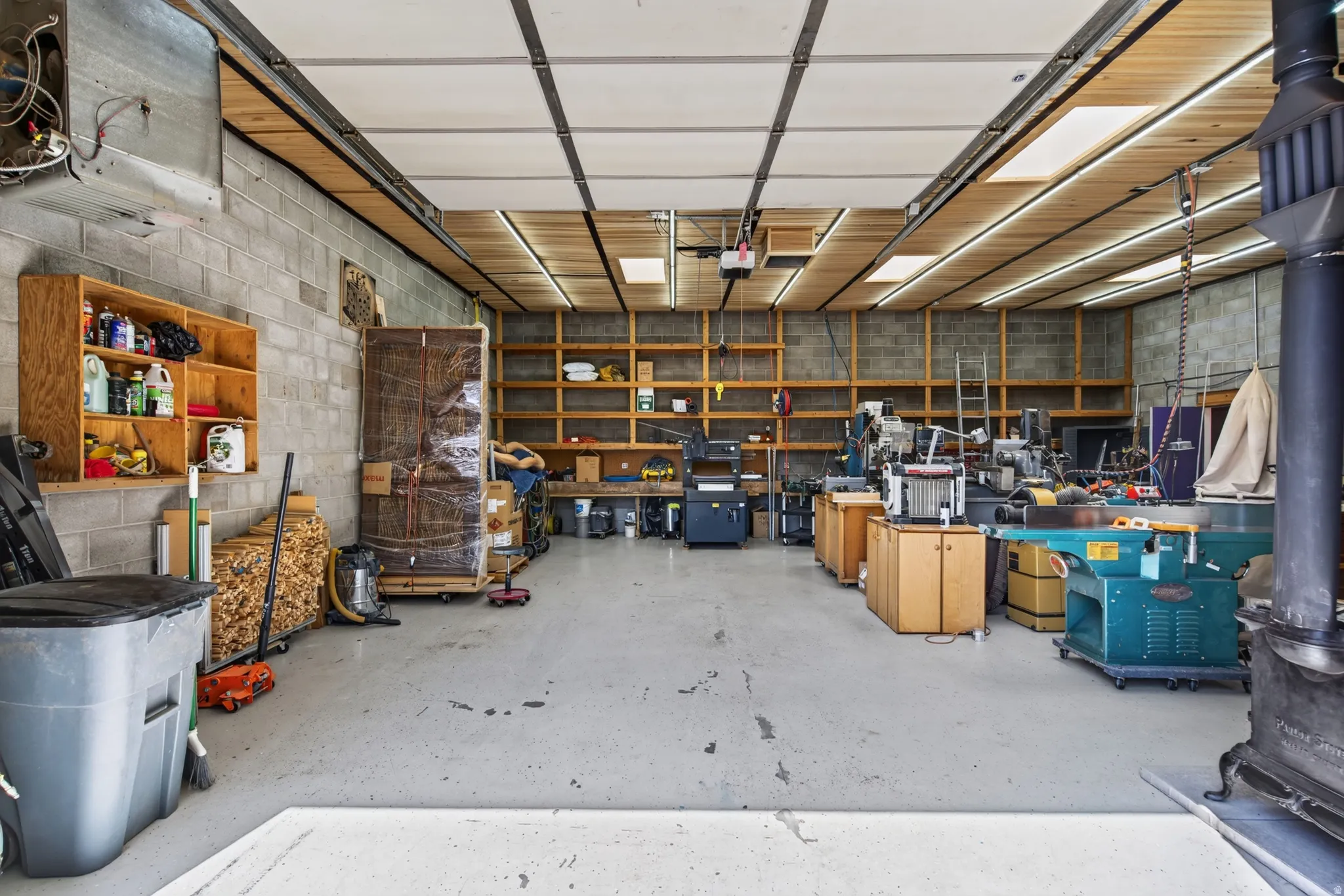 Spacious garage with concrete flooring, block walls, extensive built-in shelving, wood-paneled ceiling with recessed lighting, and skylights