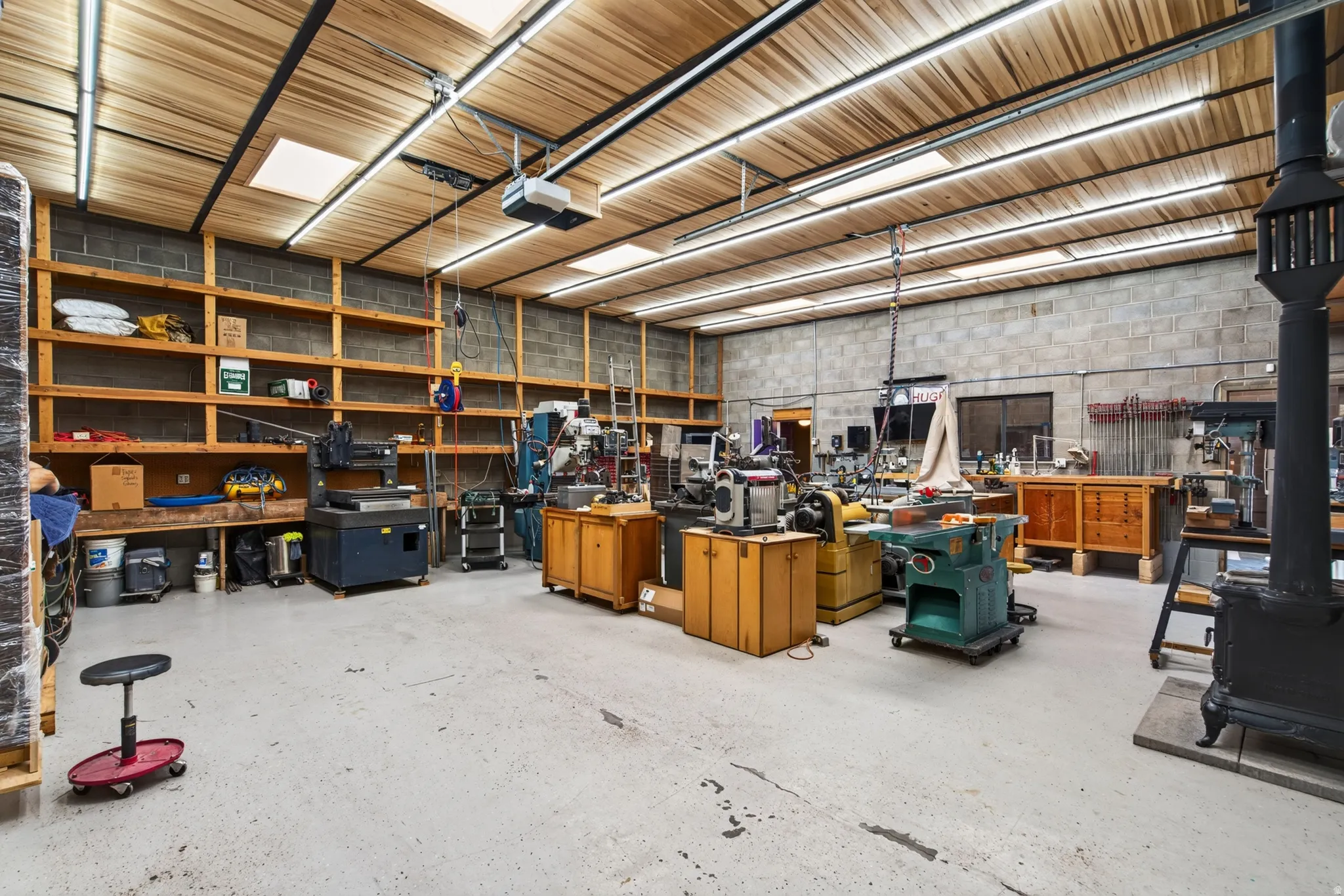 Spacious workshop featuring a wood-plank ceiling, exposed concrete block walls, and extensive built-in wooden shelving