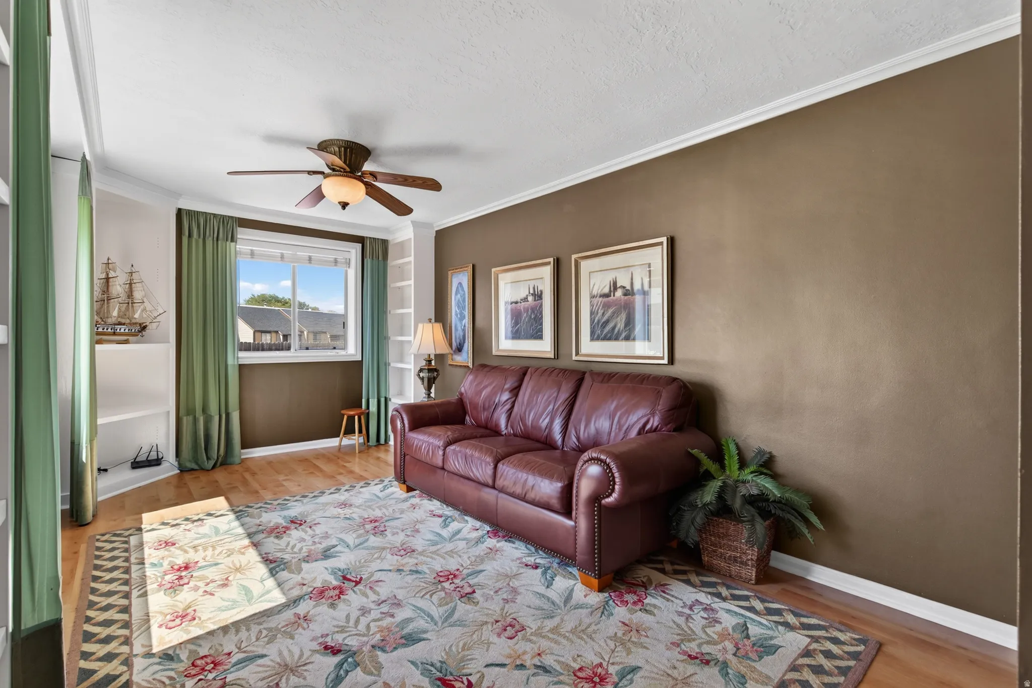 Living area featuring wood-finish flooring, a ceiling fan with integrated lighting, and crown molding