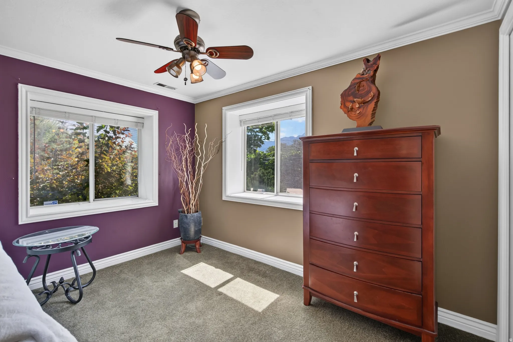 Bright interior room featuring a ceiling fan with integrated lighting, two windows with white trim, crown molding, and carpeted flooring
