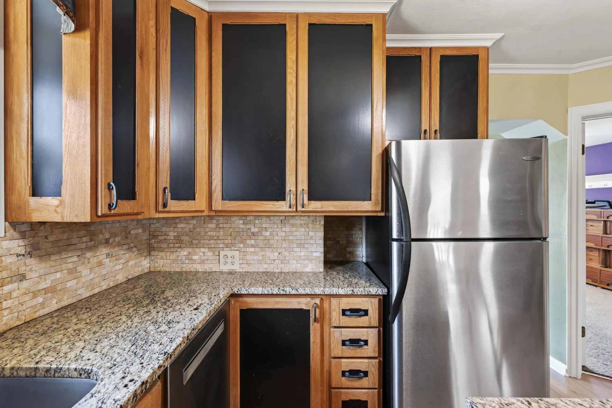 Kitchen featuring natural wood cabinetry, light-toned granite countertops, a tiled backsplash, and stainless steel appliances
