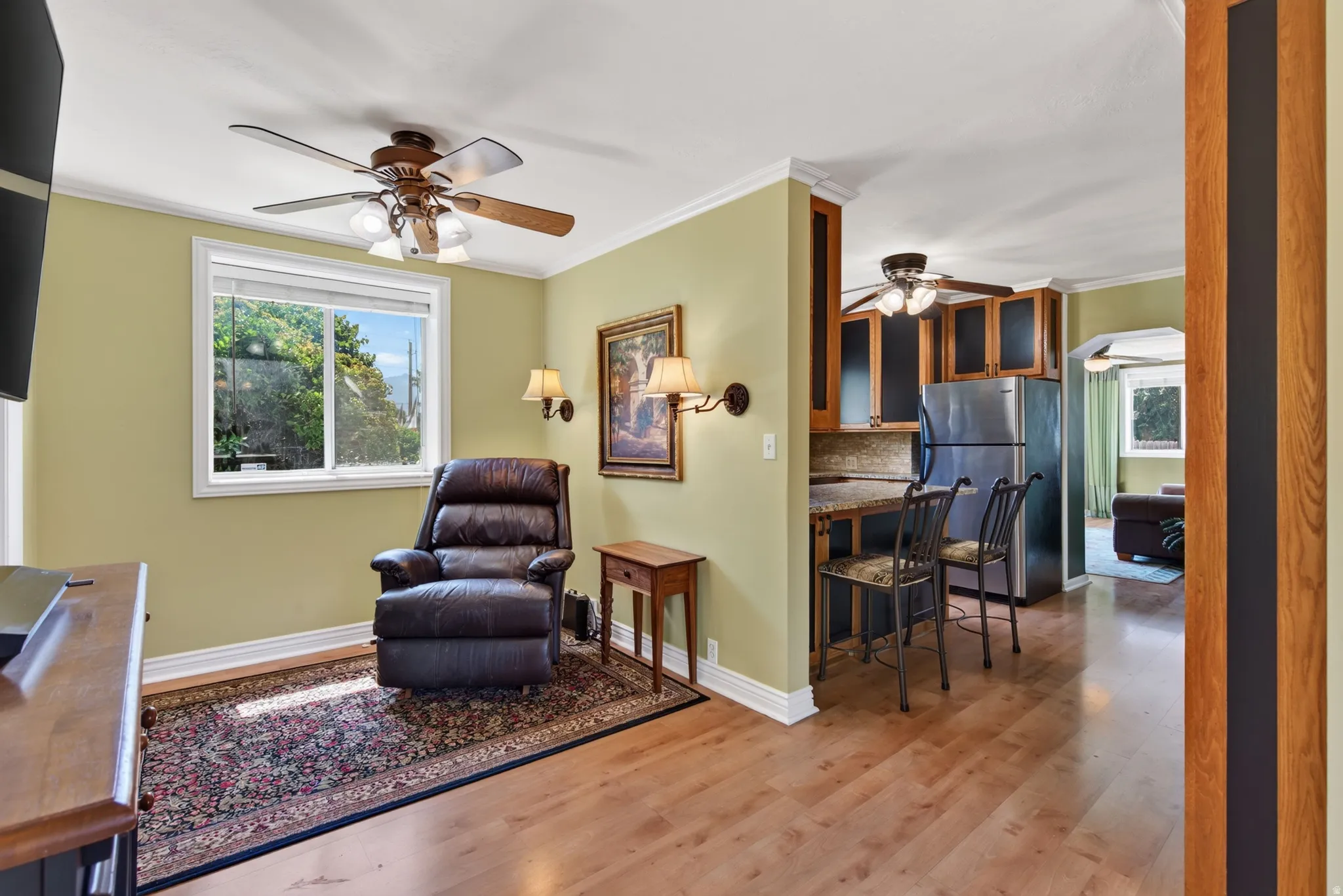 Open-concept living area featuring wood-finish flooring, a contemporary ceiling fan, and a kitchen pass-through with breakfast bar seating