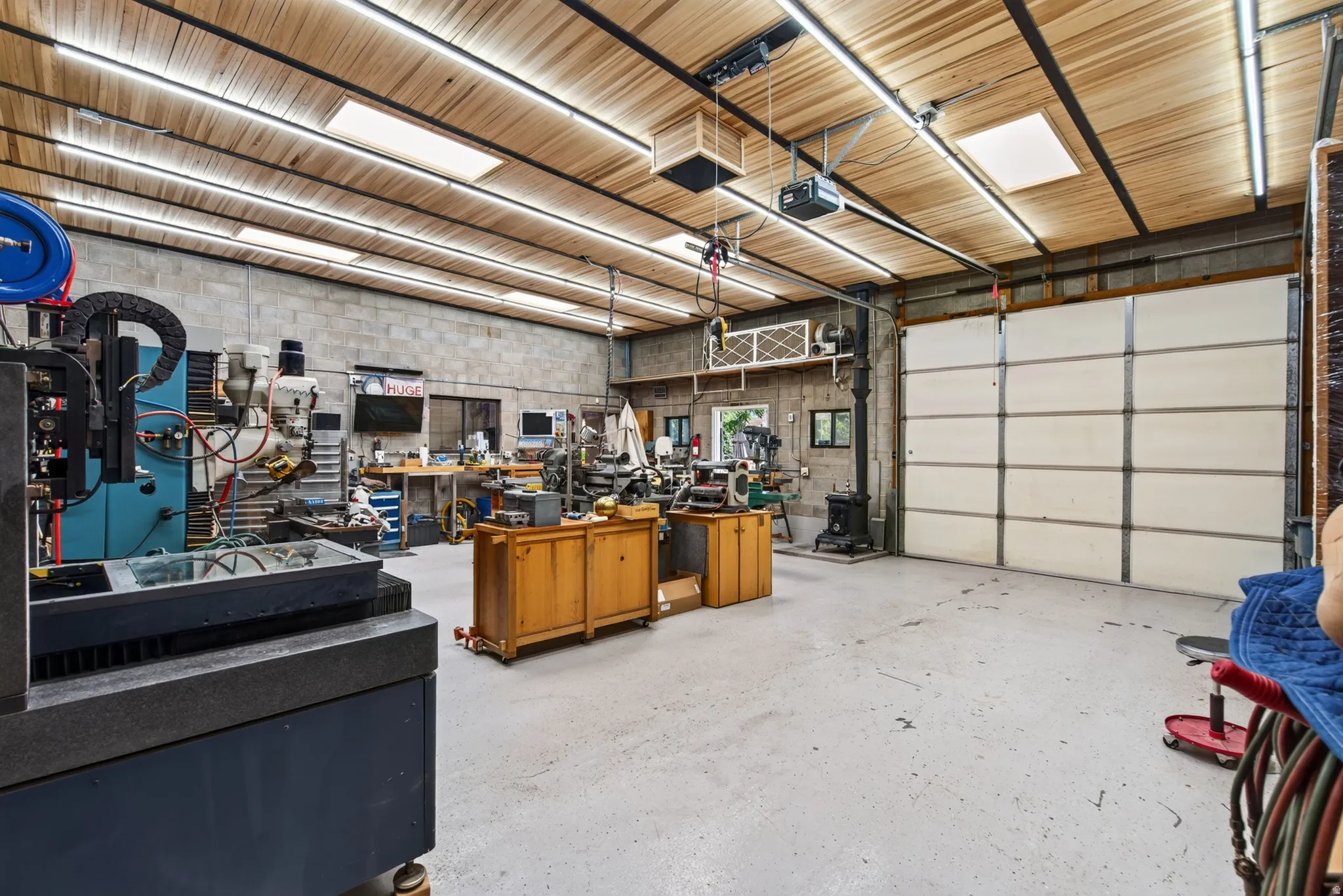 Expansive workshop space featuring a paneled ceiling with integrated lighting, concrete block walls, and a large overhead garage door