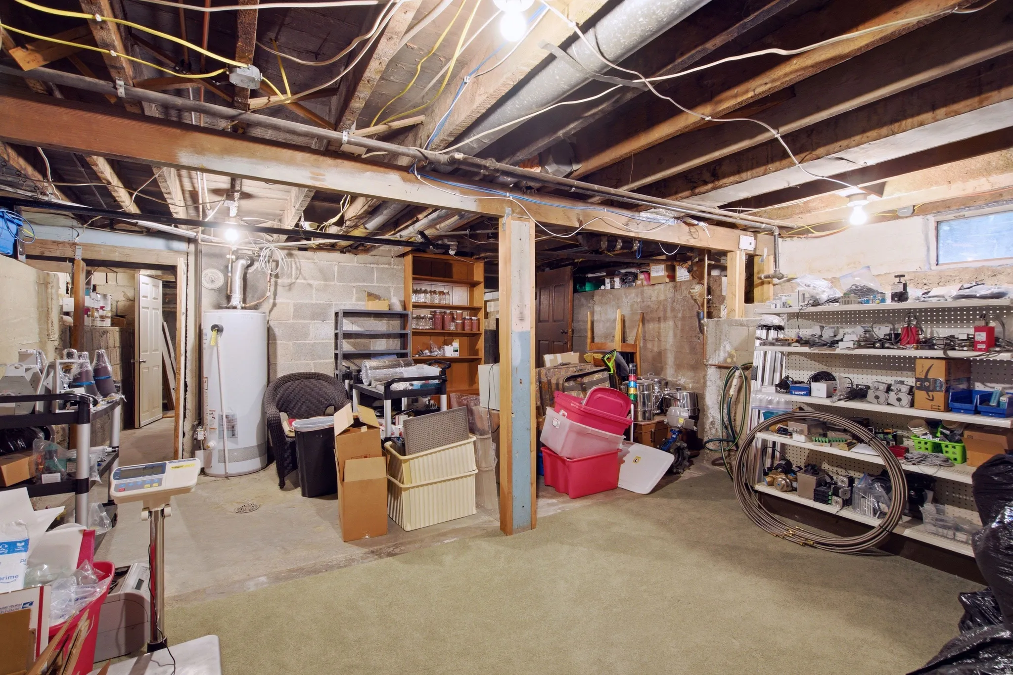Unfinished basement space featuring exposed wood joists, concrete block walls, and a water heater