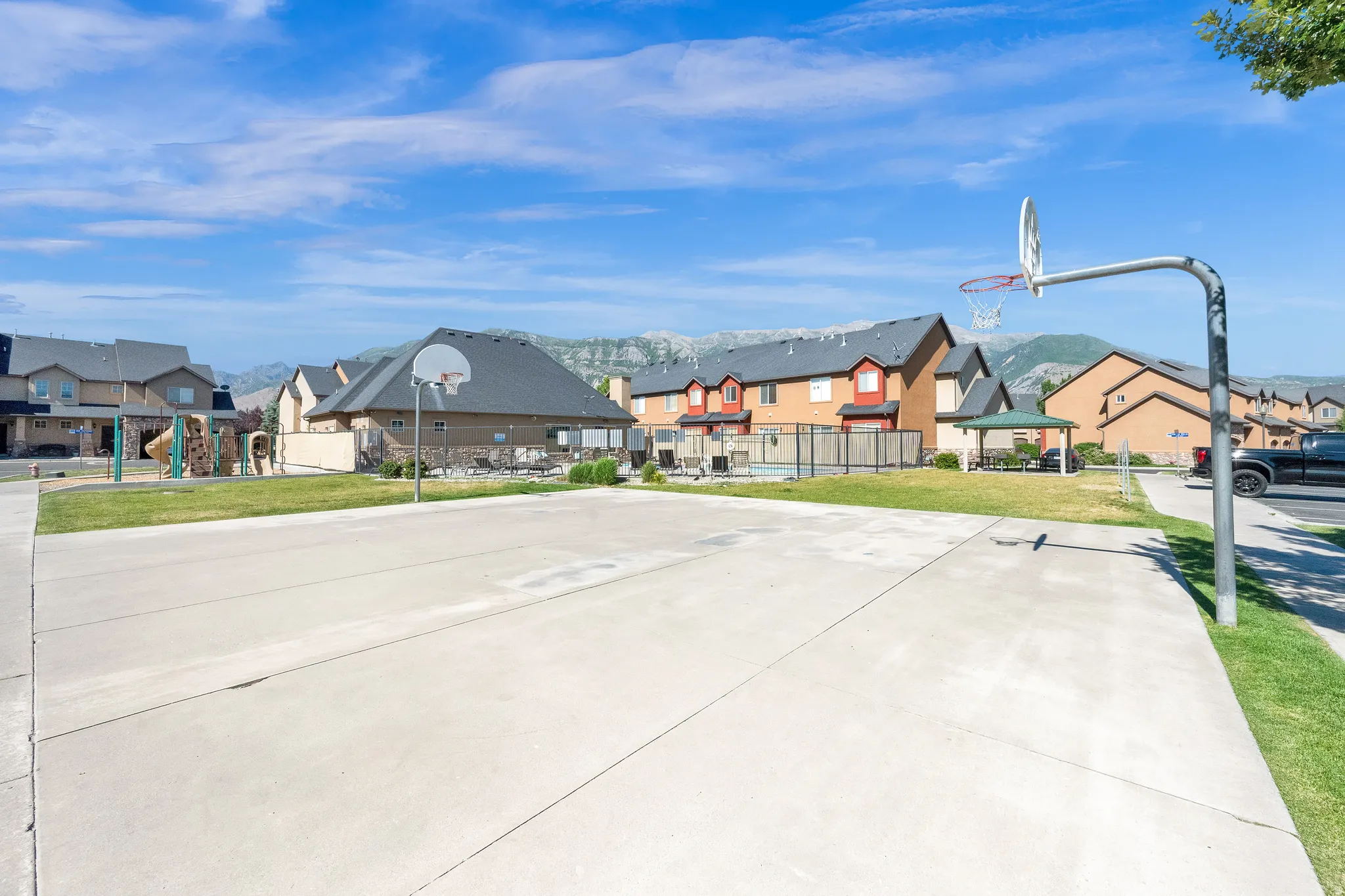 Paved basketball court with a metal hoop, surrounded by green lawns and residential buildings