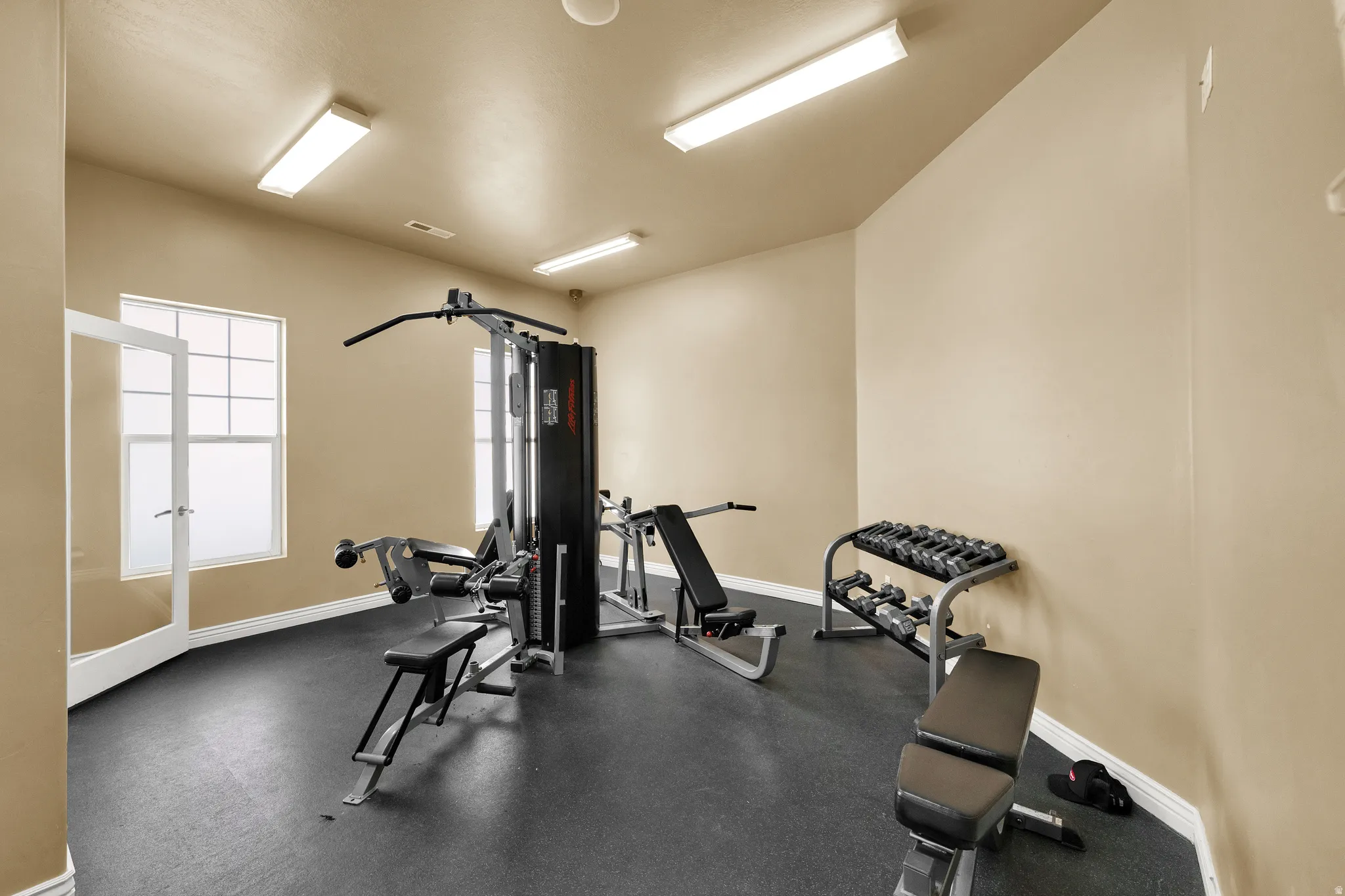 Dedicated exercise room featuring dark rubber flooring, light beige wall paint, and multiple rectangular windows