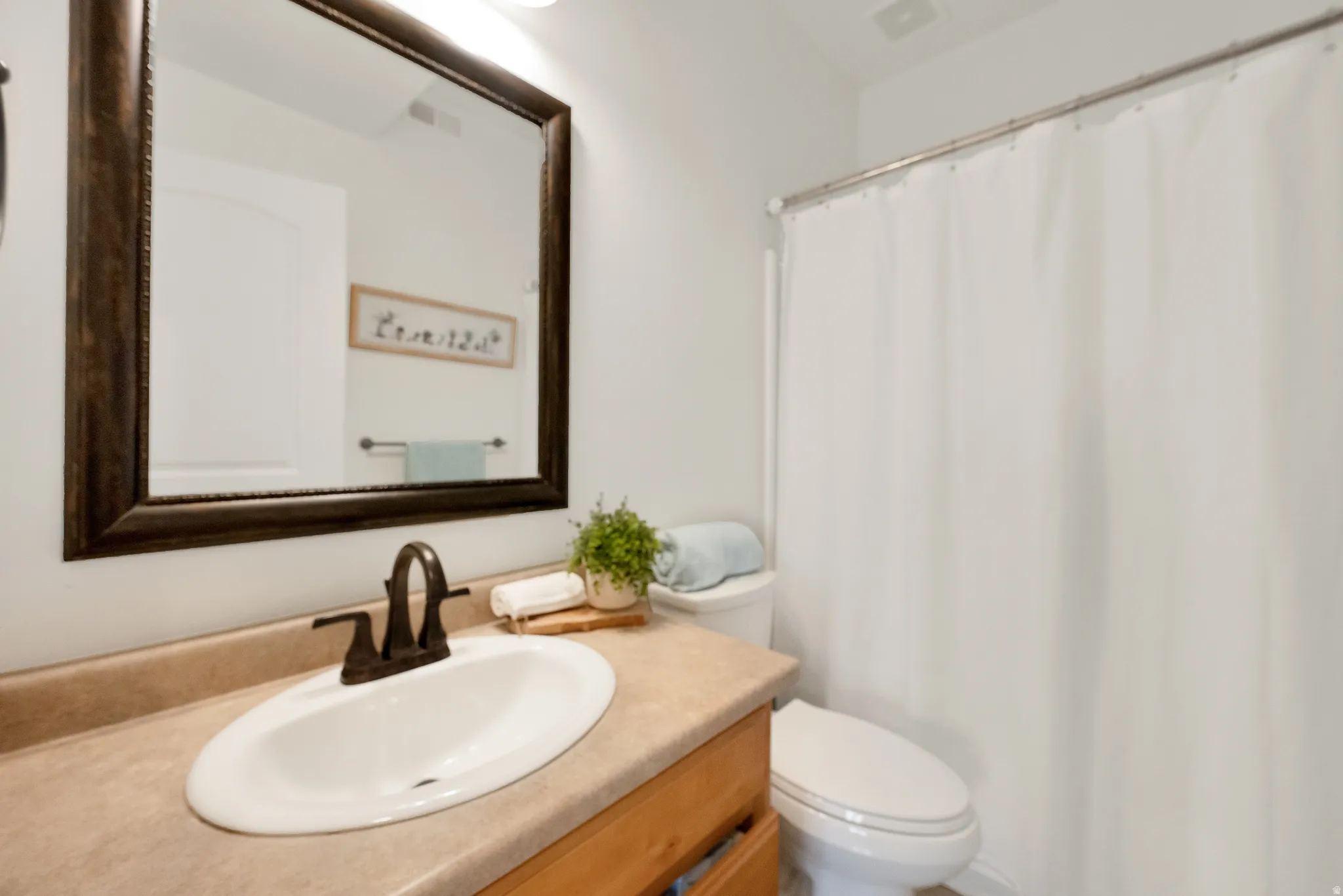 Full bathroom featuring a rectangular vanity mirror with a dark wood-finish frame, a light wood-finish vanity cabinet, and a shower/tub combination with a white curtain