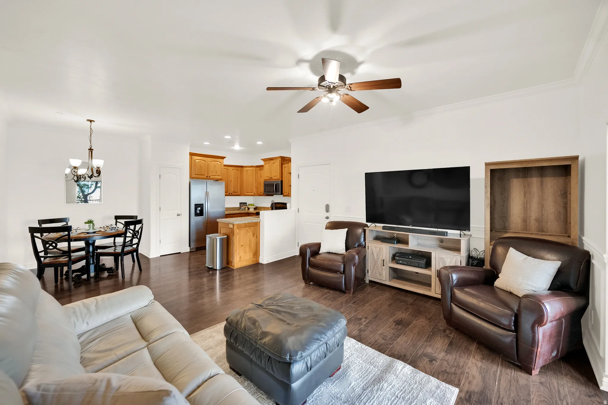 Open-concept living space featuring wood-finish flooring, a dining area with chandelier lighting, a kitchen with wood cabinetry and stainless steel appliances, and a ceiling fan