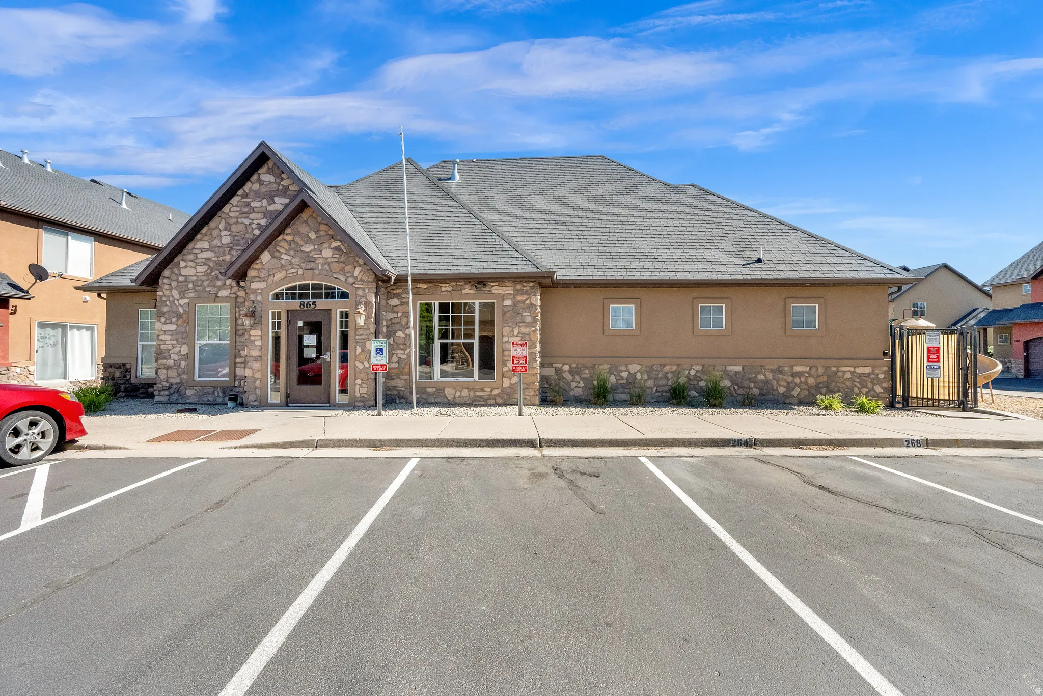 Community building with stone and stucco exterior, arched entryway, a prominent gable roof, and a paved parking area