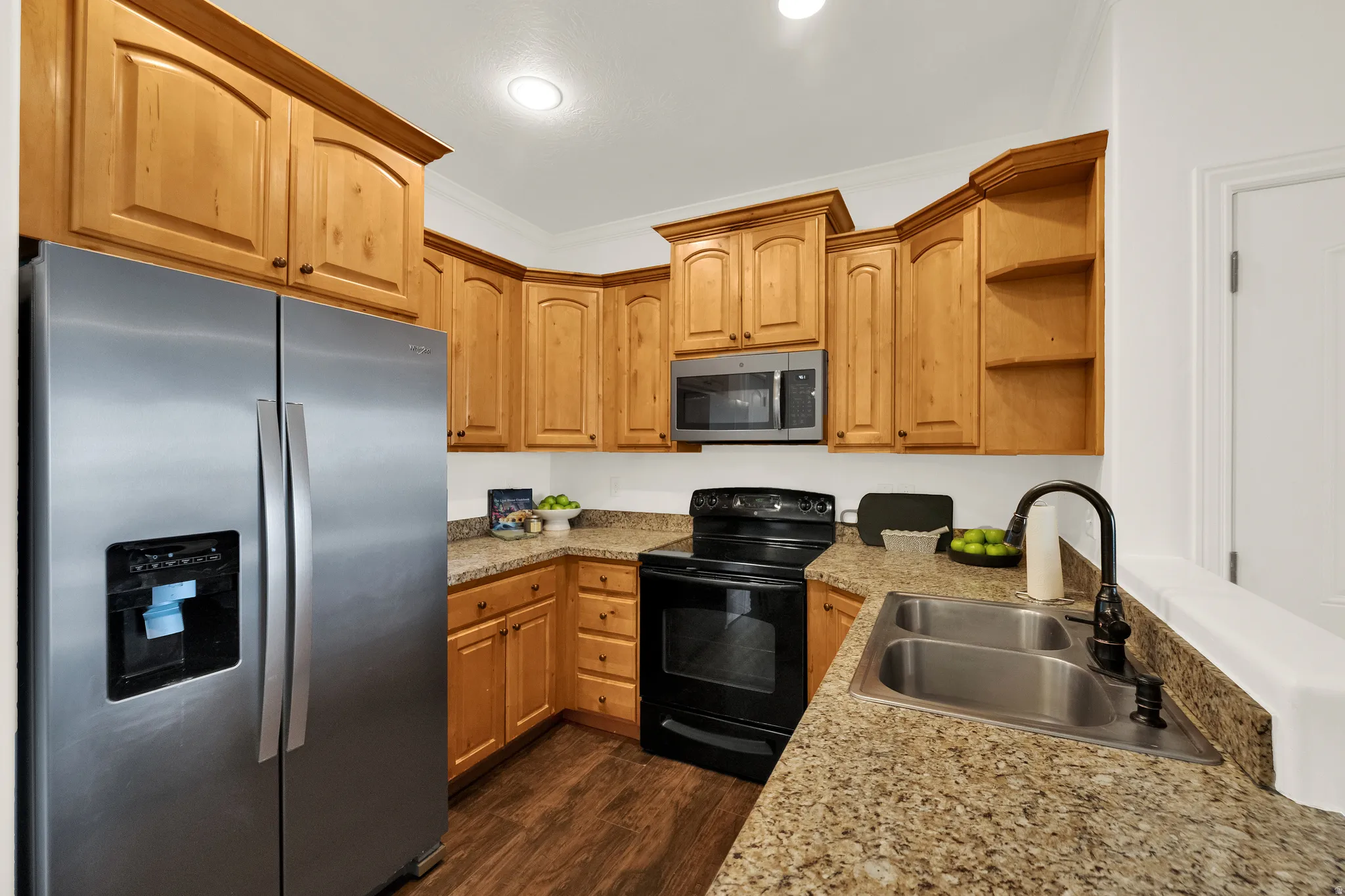 Kitchen featuring wood-finish cabinetry, granite-style countertops, wood-finish flooring, a stainless steel refrigerator, and a double basin sink with a matte black faucet