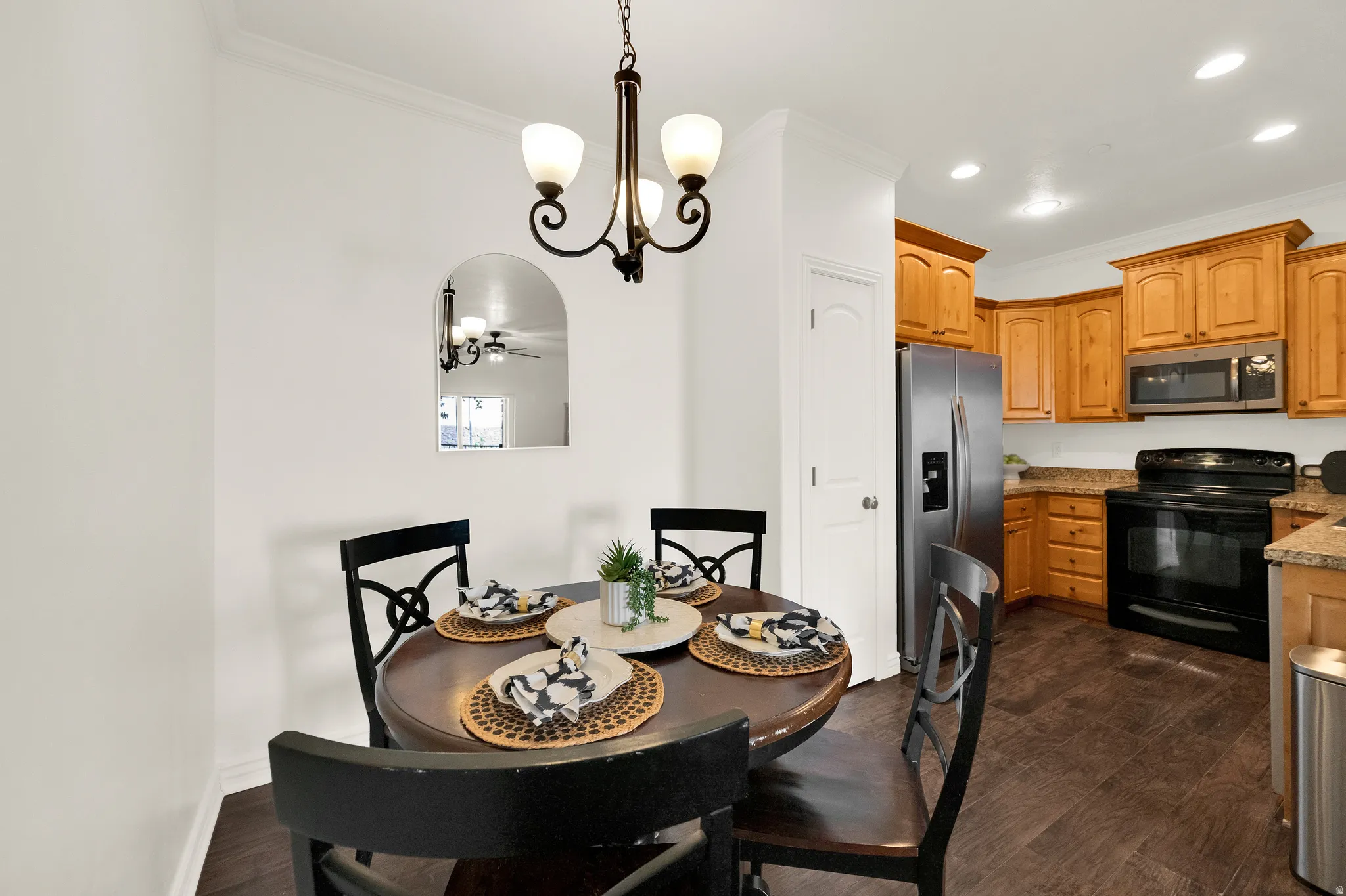 Open-concept kitchen and dining area featuring wood-finish flooring, recessed lighting, wood cabinetry, and stainless steel appliances including a refrigerator, microwave, and range