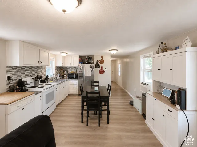 Kitchen featuring white cabinetry with dark hardware, tile backsplash, a stainless steel refrigerator, and wood-finish flooring