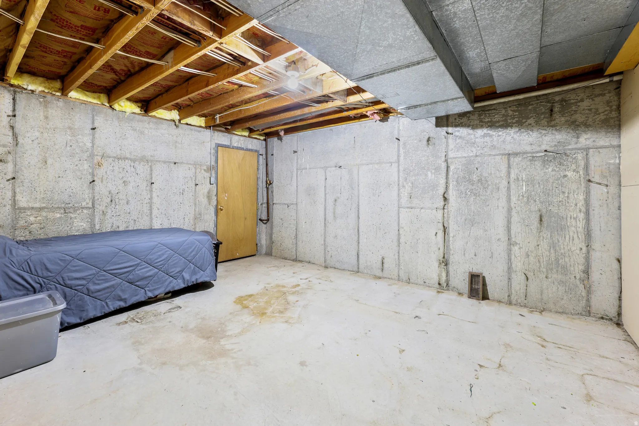 Unfinished basement space featuring exposed concrete walls and floor, visible ceiling joists, and ductwork