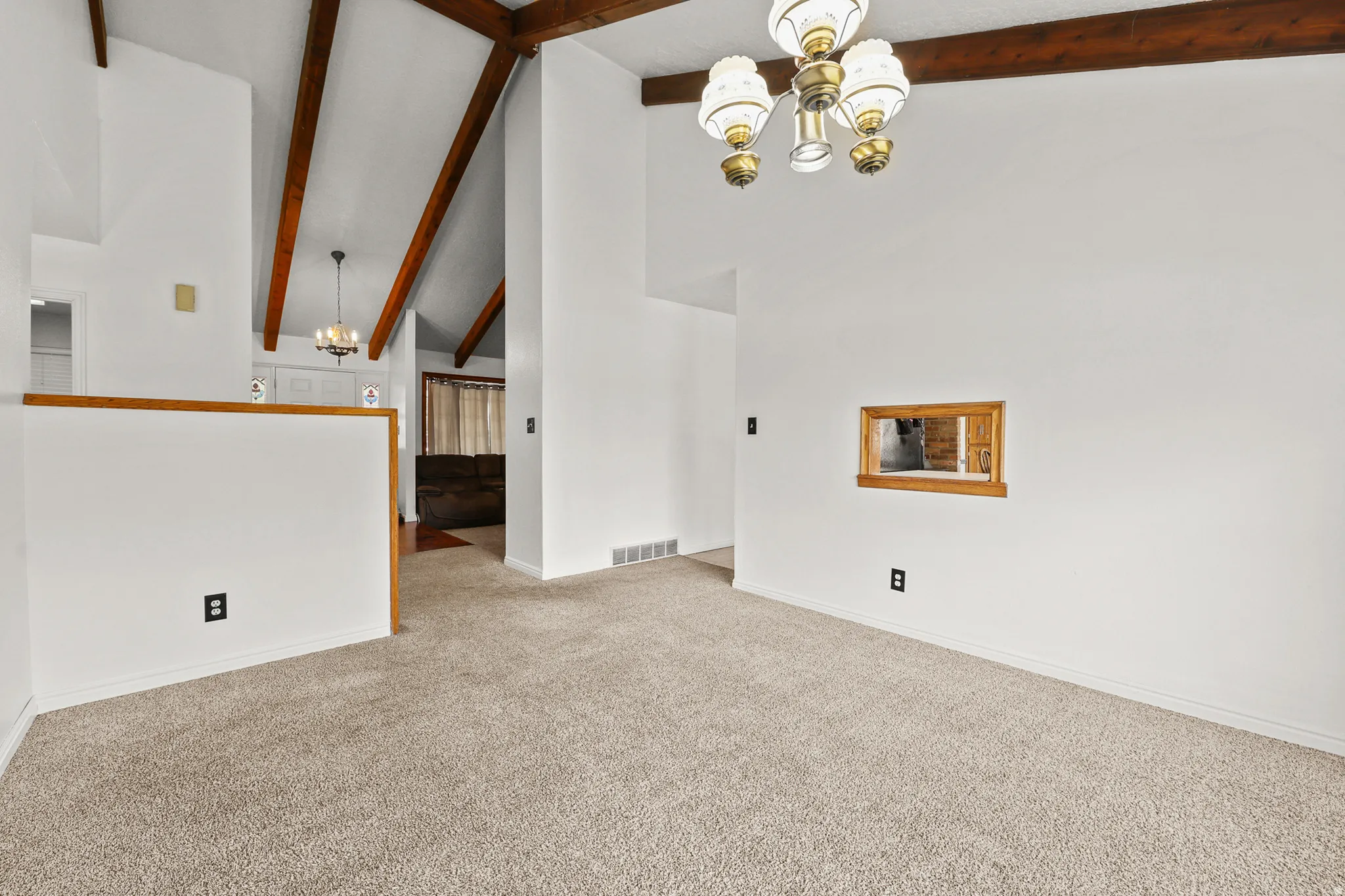 Vaulted ceilings with exposed wood beams, neutral carpeting, and a decorative chandelier