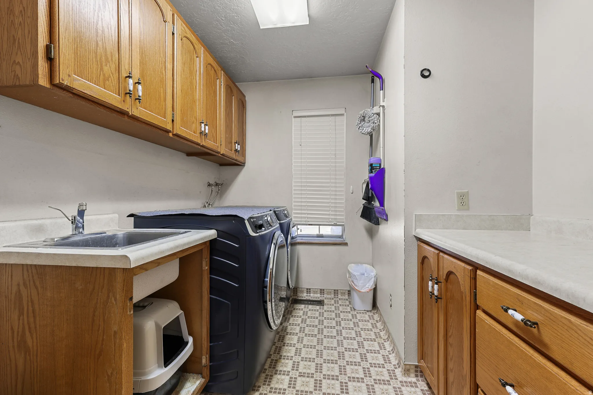 Utility room featuring a built-in sink with a countertop, wood cabinetry, and patterned floor tile