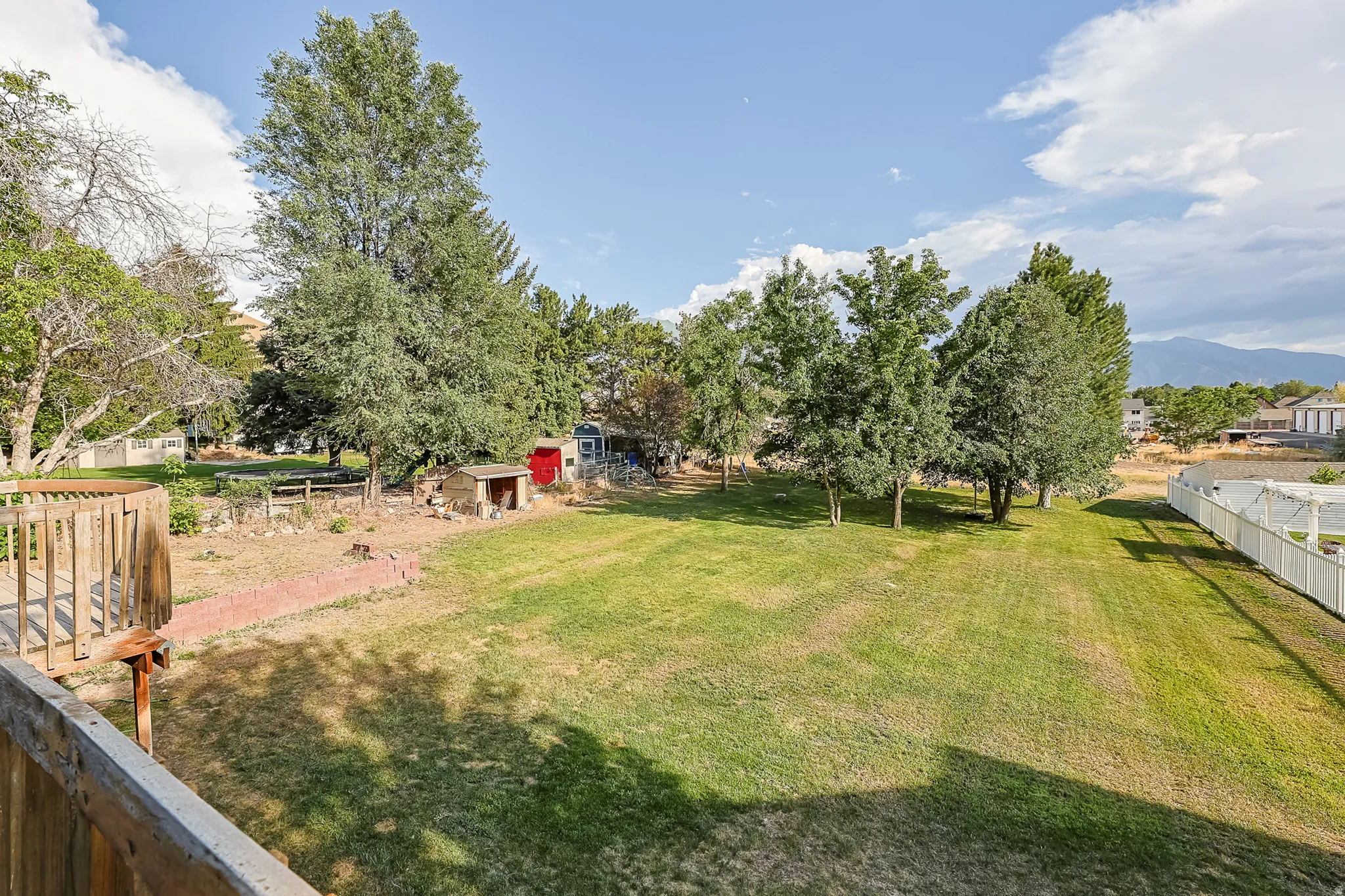 Expansive backyard featuring a large grassy area, mature trees, and a white picket fence