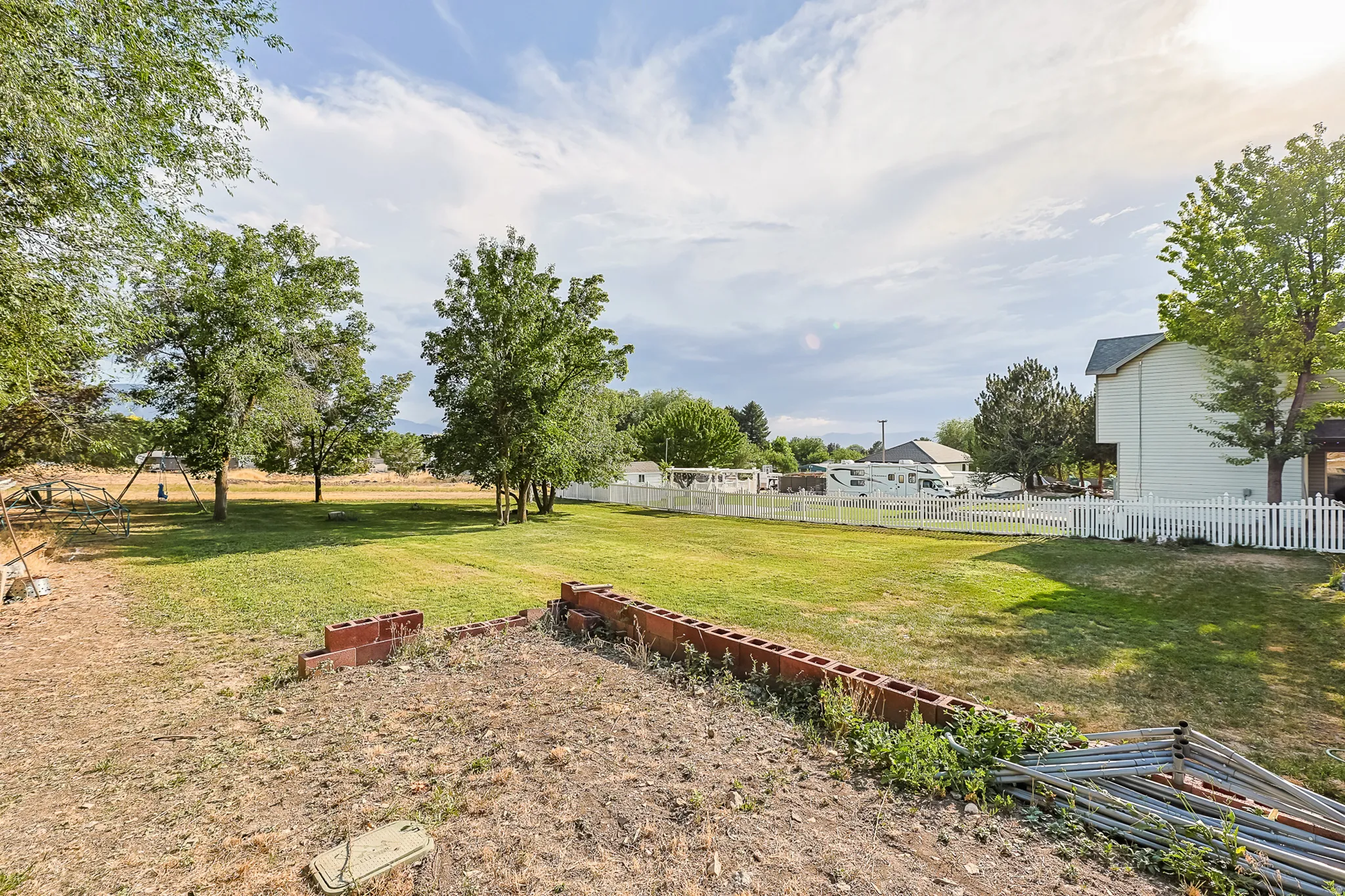 Expansive exterior space featuring a large grassy lawn, mature trees, a white picket fence, and a partial retaining wall