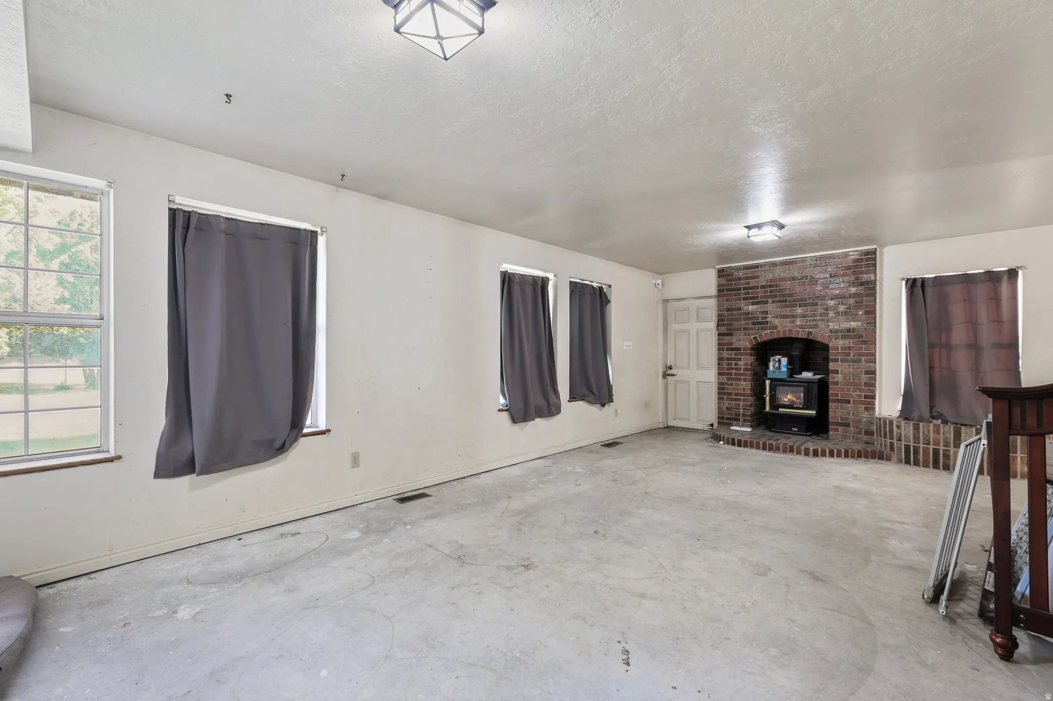 Spacious room featuring multiple windows, a prominent brick fireplace with a wood-burning stove insert, and a solid exterior door