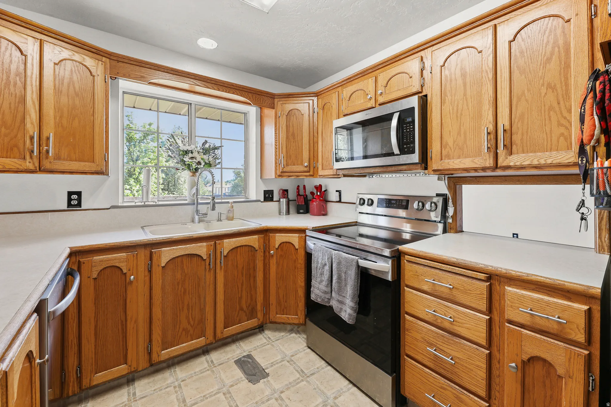 Kitchen featuring wood cabinetry, light-toned countertops, a stainless steel microwave, and a stainless steel electric range