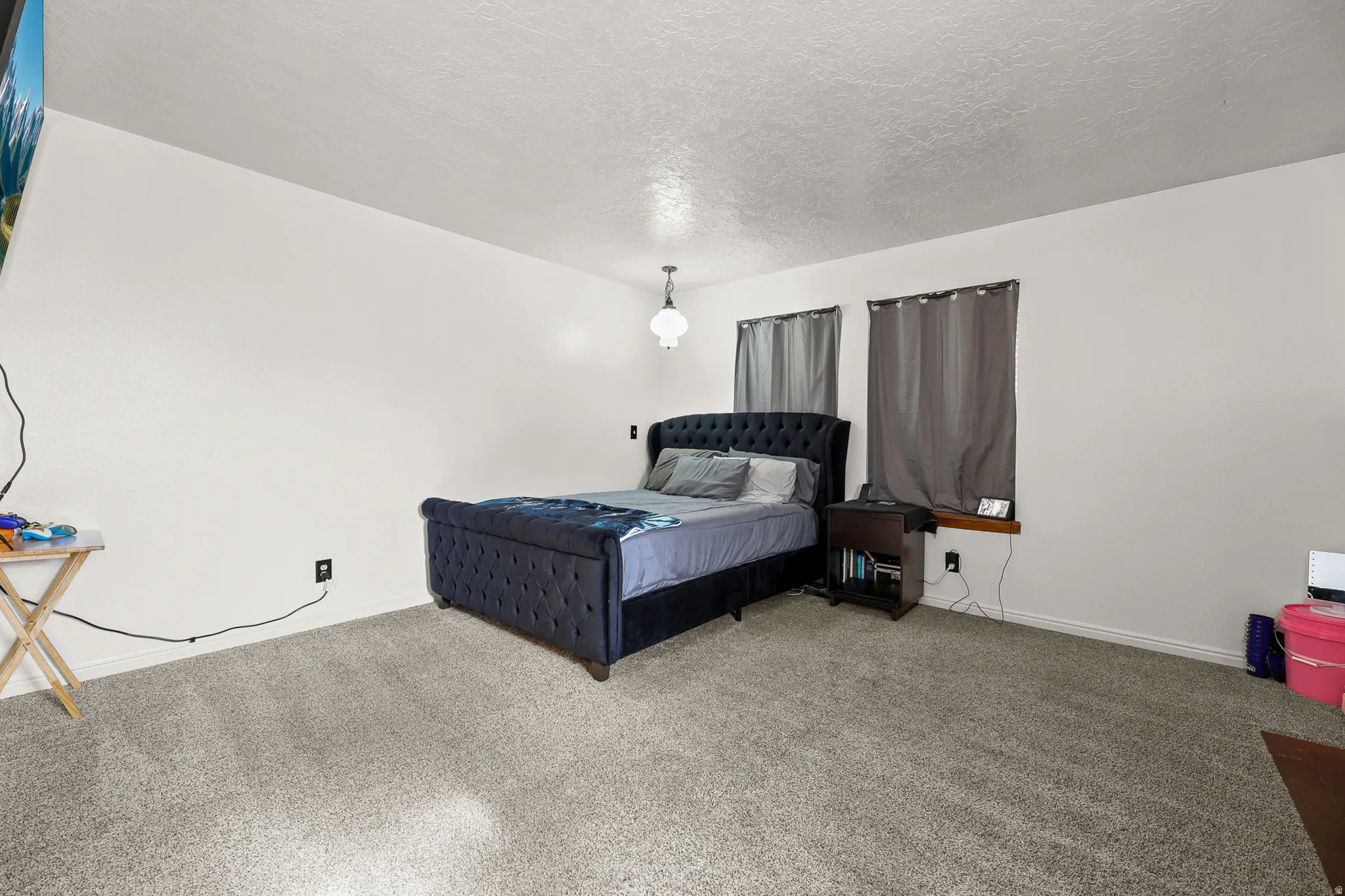 Carpeted room with a ceiling-mounted light fixture, white walls, and two windows featuring dark curtains
