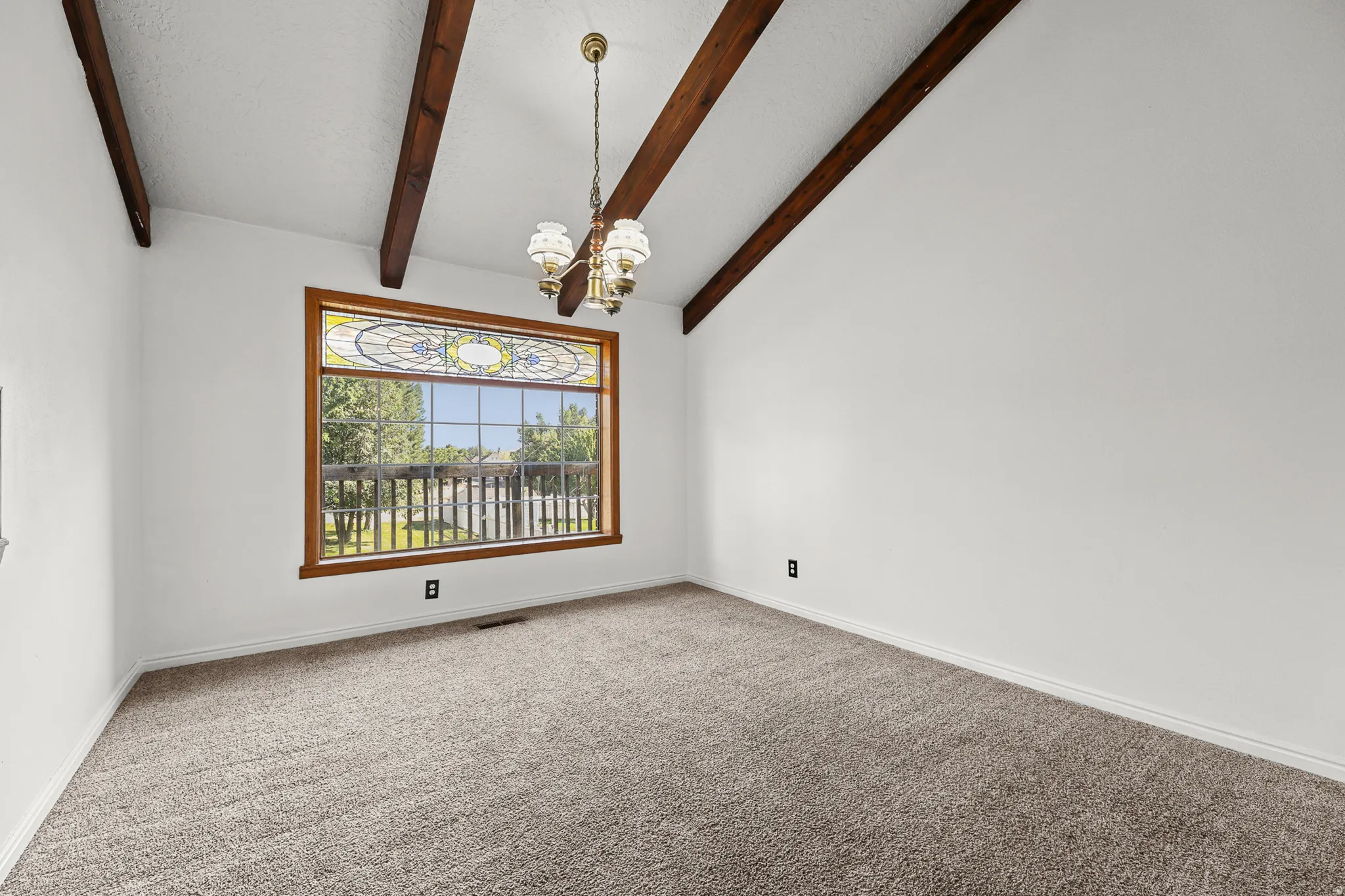 Vaulted ceiling featuring exposed wood beams, a decorative chandelier, and a large window with stained glass detail