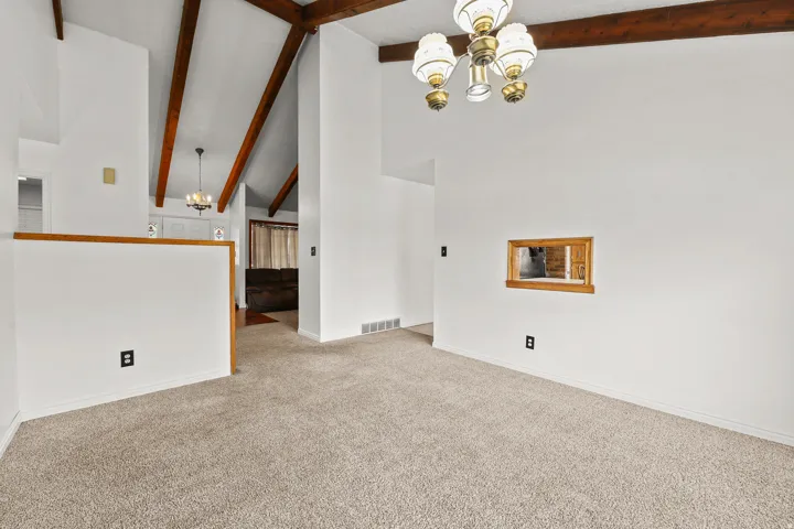 Vaulted ceilings with exposed wood beams, neutral carpeting, and a decorative chandelier