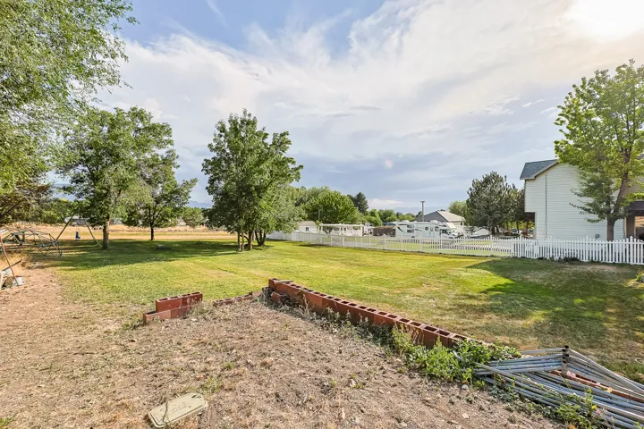 Expansive exterior space featuring a large grassy lawn, mature trees, a white picket fence, and a partial retaining wall
