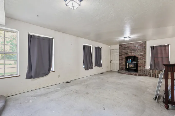 Spacious room featuring multiple windows, a prominent brick fireplace with a wood-burning stove insert, and a solid exterior door