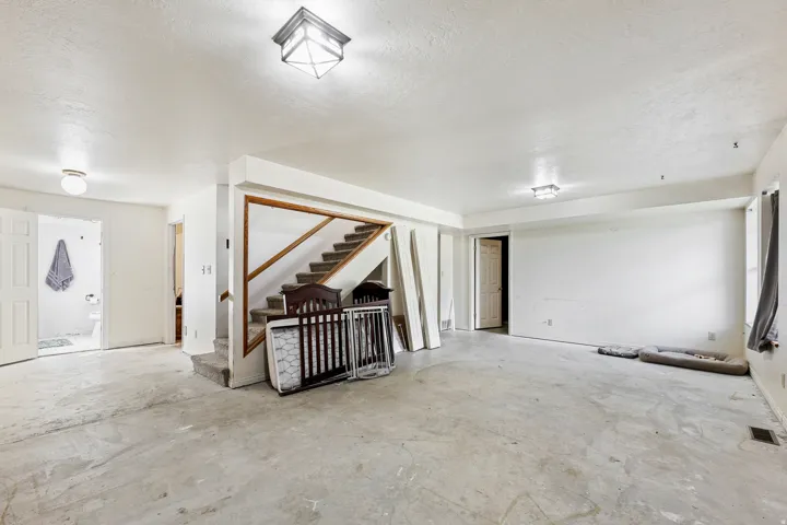 Spacious lower-level room featuring an exposed concrete floor, white walls, and a staircase with wood railing