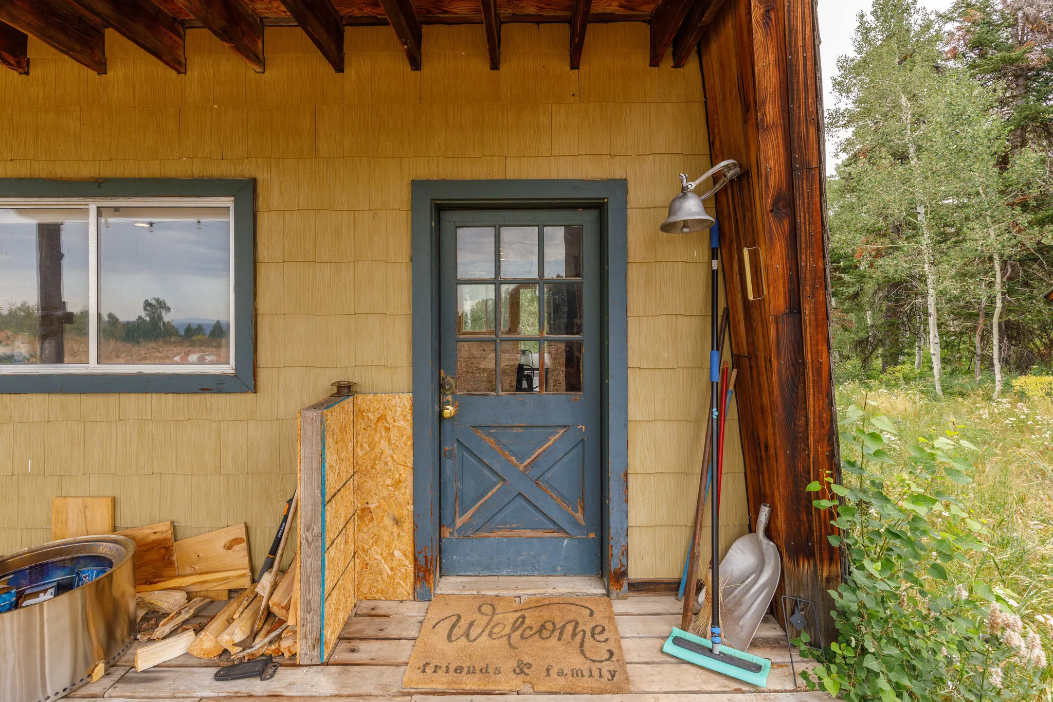 Front entrance featuring a blue paneled door with glass inserts, yellow siding, a prominent wood column, and a wooden porch
