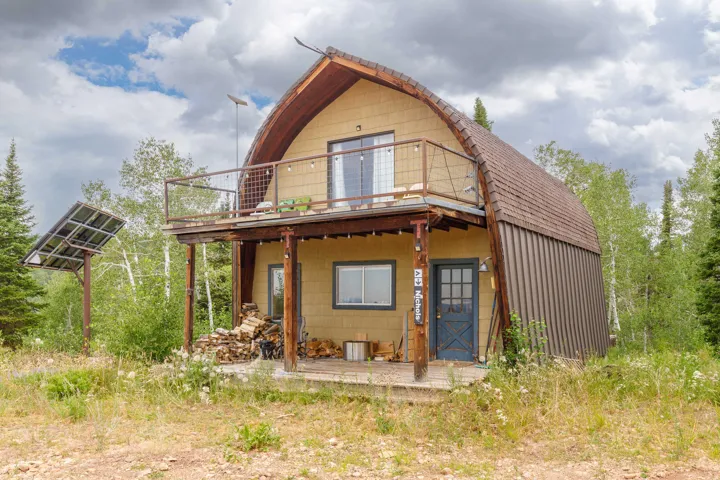 Barn-style architecture featuring a second-story balcony with metal railing, an outdoor solar panel array, and a ground-level covered porch