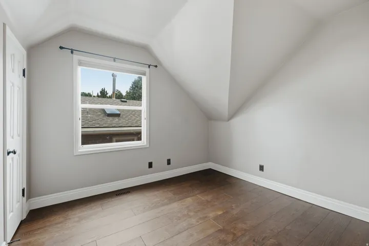 Room featuring wood-finish flooring, white baseboards, and light gray walls with sloped ceilings