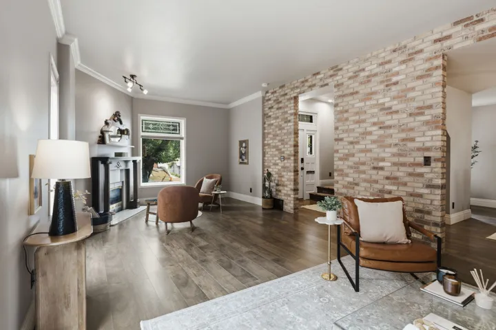 Open-concept living space featuring wood-finish flooring, a brick accent wall, a fireplace with a black mantel, and crown molding
