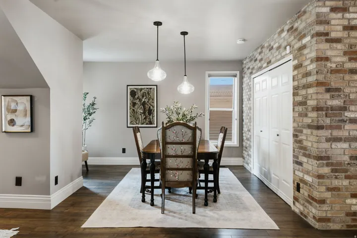 Dining area featuring dark wood-finish flooring, light grey walls, and a prominent brick accent wall