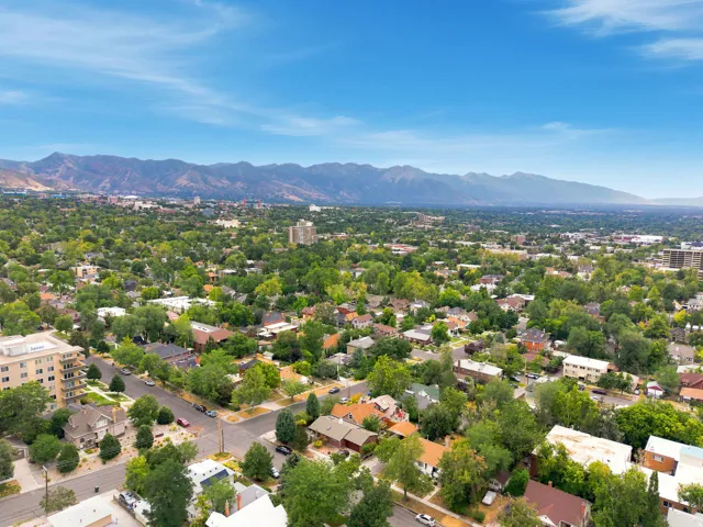 Expansive urban landscape featuring a mix of residential and commercial buildings, mature trees, and mountainous scenery