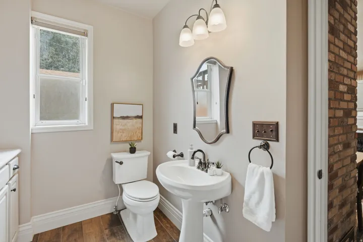 Pedestal sink with dark-finish faucet, framed mirror, and three-light vanity fixture
