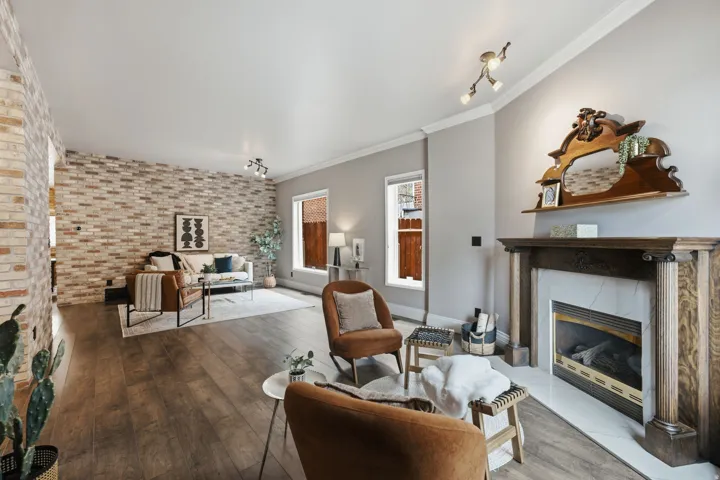 Spacious living area featuring wood-finish flooring, a brick accent wall, and a fireplace with a wood mantle and marble surround
