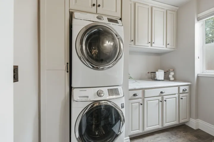 Dedicated laundry space featuring a stacked washer and dryer, white shaker-style cabinetry, a built-in countertop, and a window for natural light