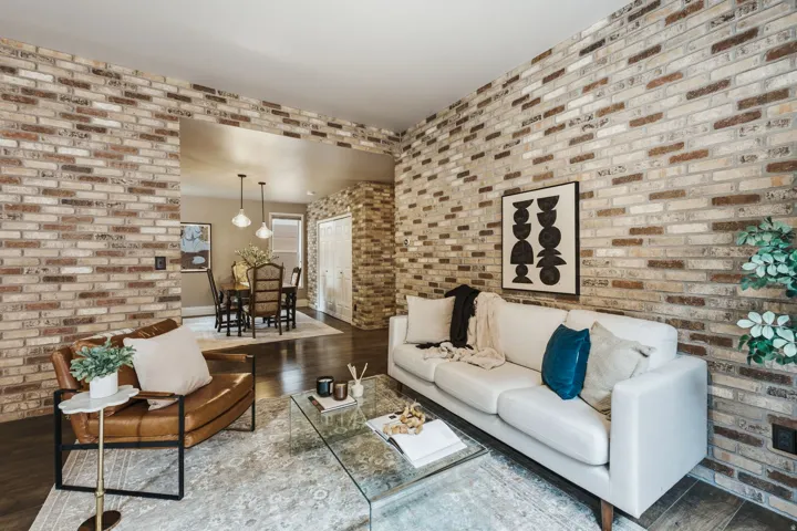 Interior living space featuring exposed brick walls, dark wood-finish flooring, and an open architectural feature to a dining area