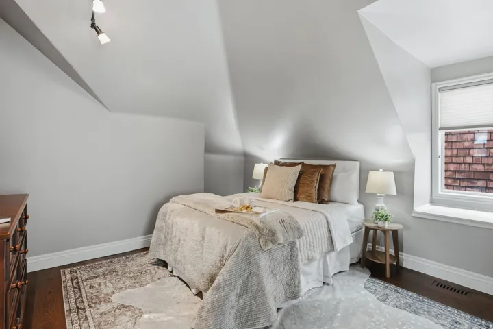 Attic bedroom featuring dark wood-finish flooring, light grey walls, and a prominent window with white trim