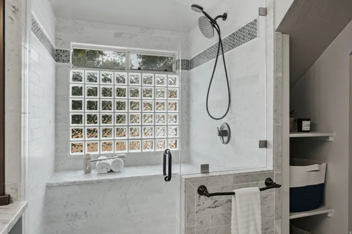 Enclosed shower featuring a clear glass door, a glass block window, and dual shower heads