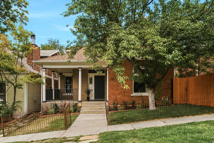 Classic brick exterior featuring a covered front porch, white columns, black railings, and a dark entry door