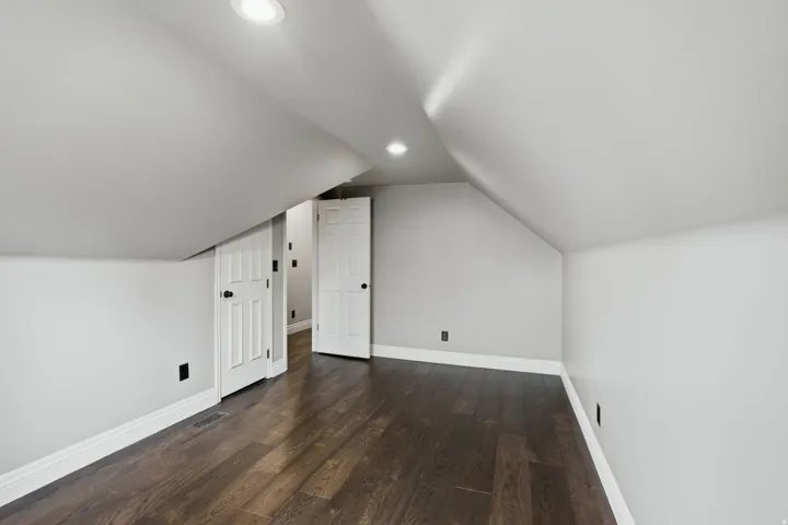 Spacious room featuring dark wood-finish flooring, recessed lighting, crisp white trim, and light gray walls