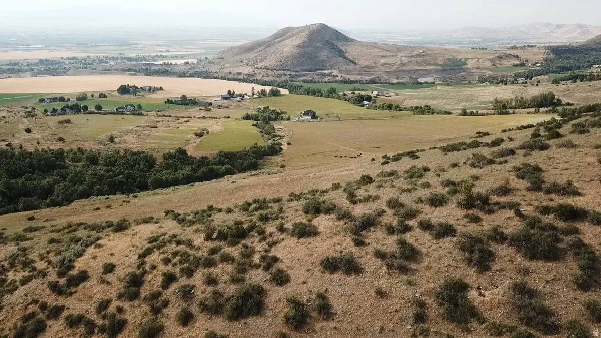 Expansive landscape showcasing a mountainous backdrop, varied topography, agricultural fields, and clusters of natural vegetation