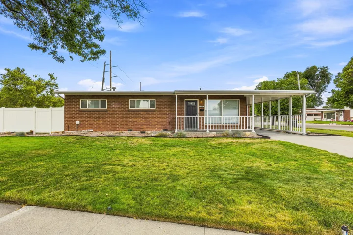 Brick exterior ranch-style residence featuring a covered front porch with white railing, an attached carport, and a paved driveway